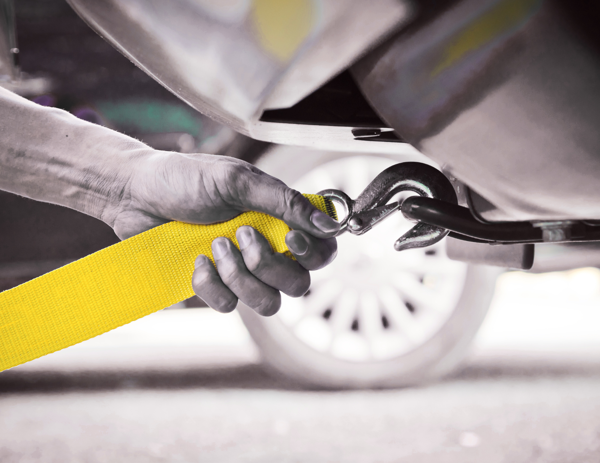 Hand attaching a yellow tow strap hook to the underside of a vehicle.