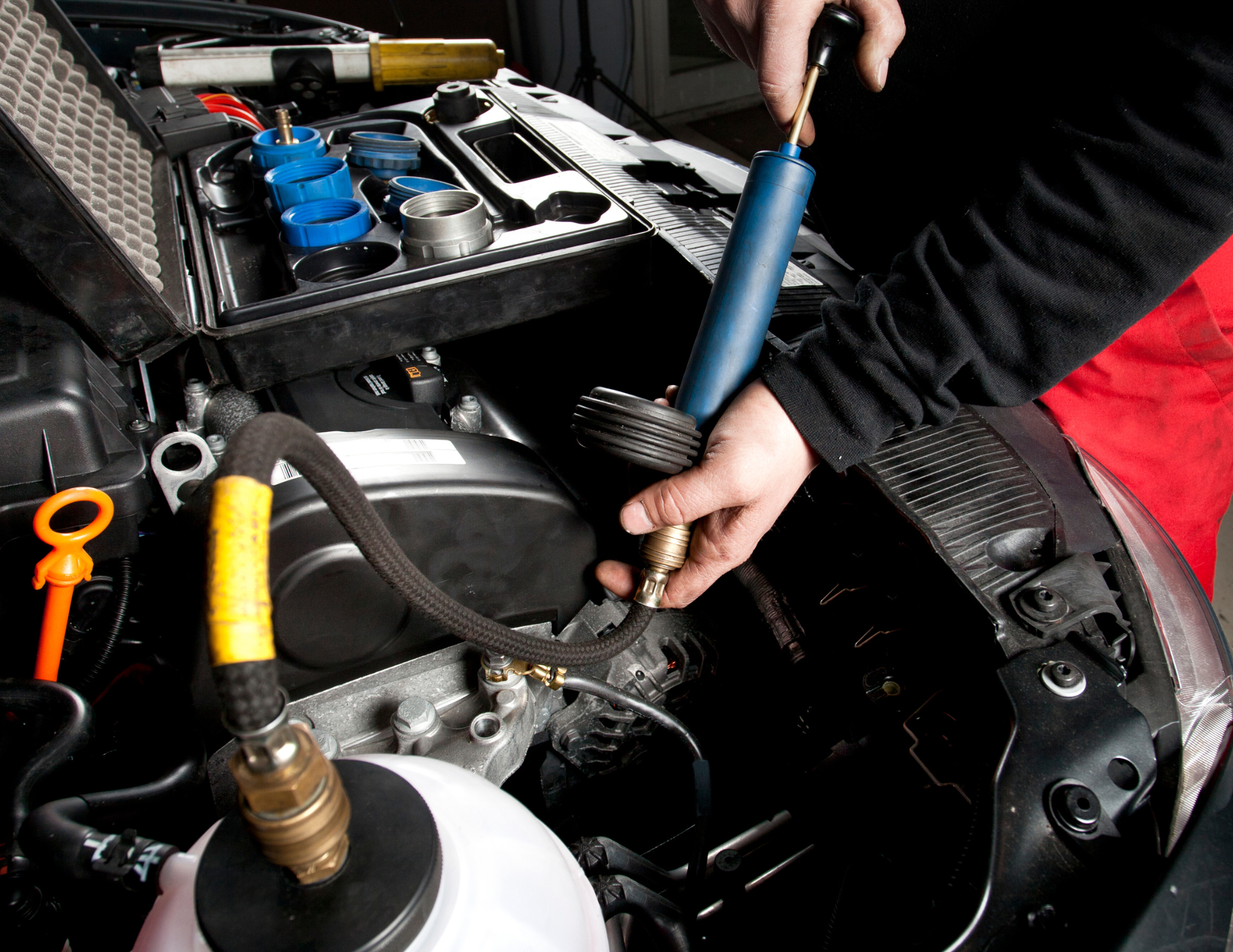 Mechanic using a tool to work on a car engine. Tools and parts are visible.