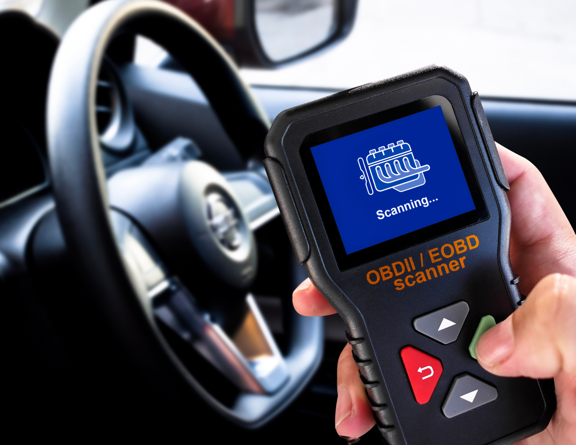 Hand holding OBD2 scanner inside a car, scanning the engine.