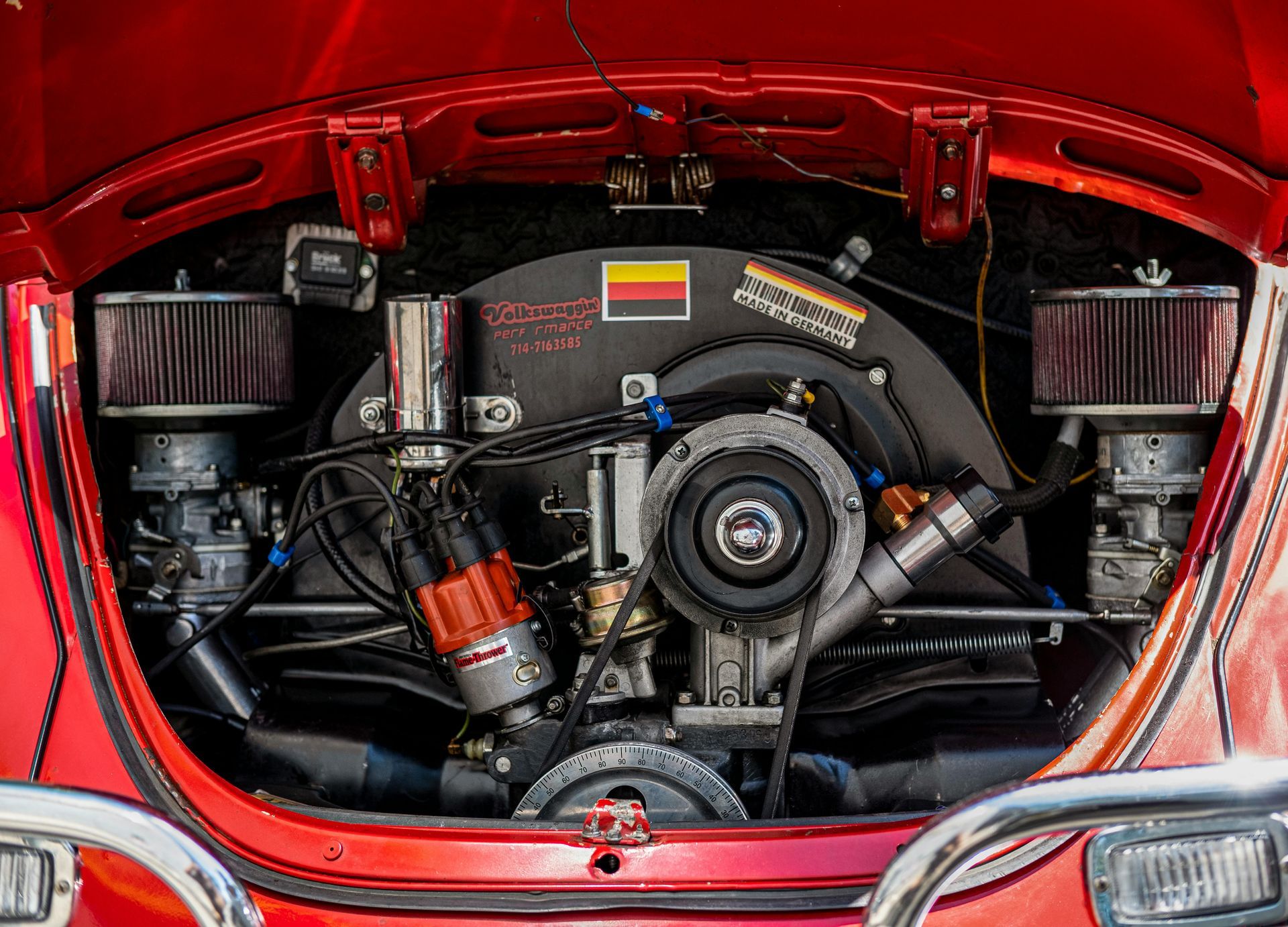 Red vintage car engine bay; engine visible with two air filters and chrome details.