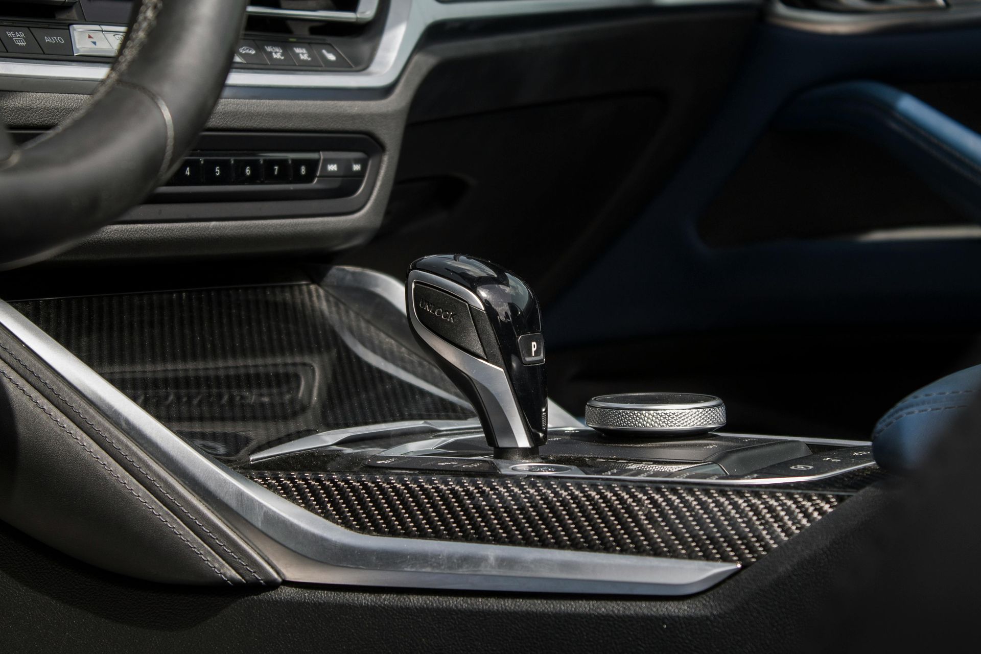 Interior car detail: gear shift lever, center console with carbon fiber trim, and infotainment dial.