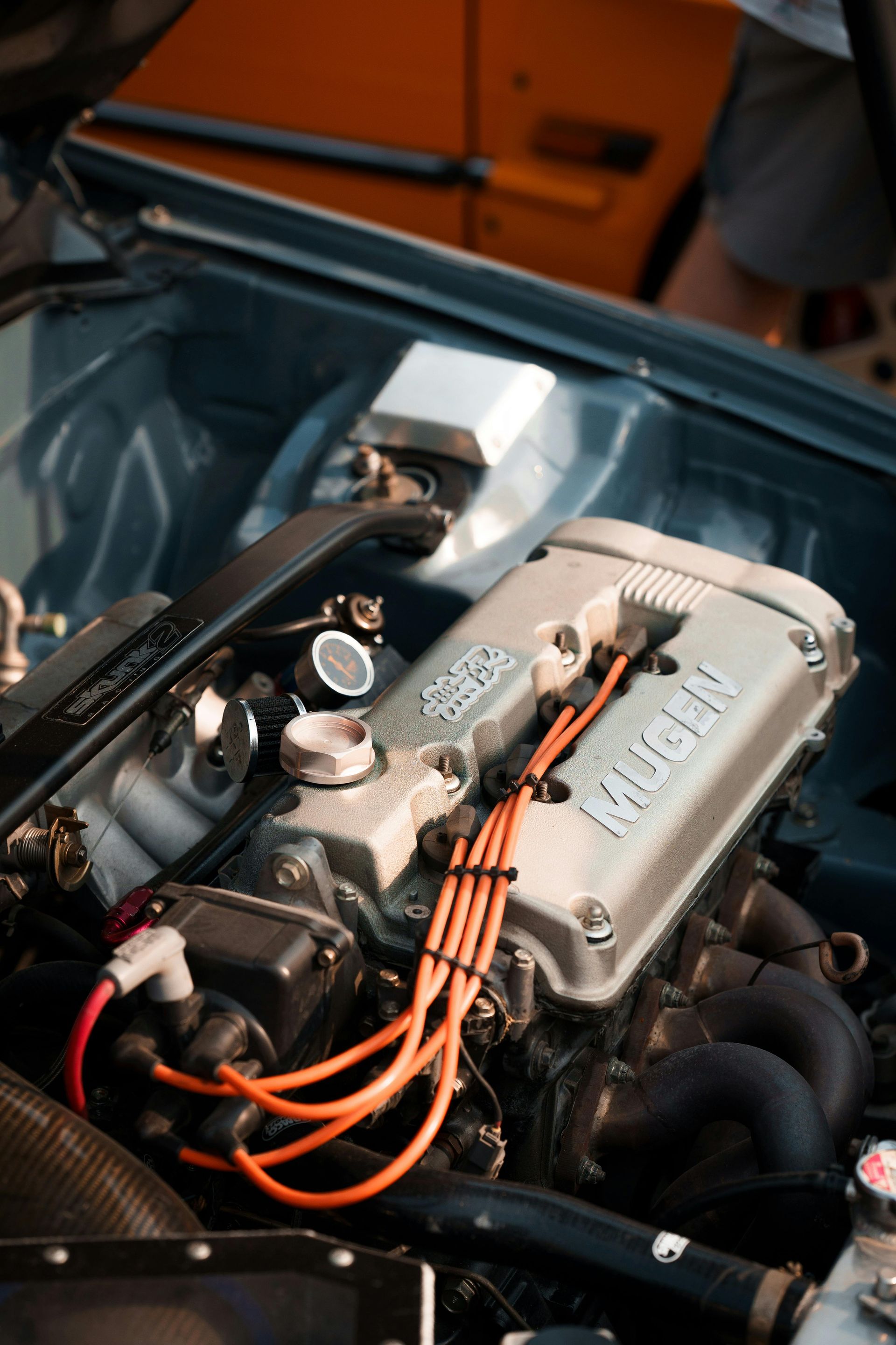 Close-up of a silver car engine with orange spark plug wires.
