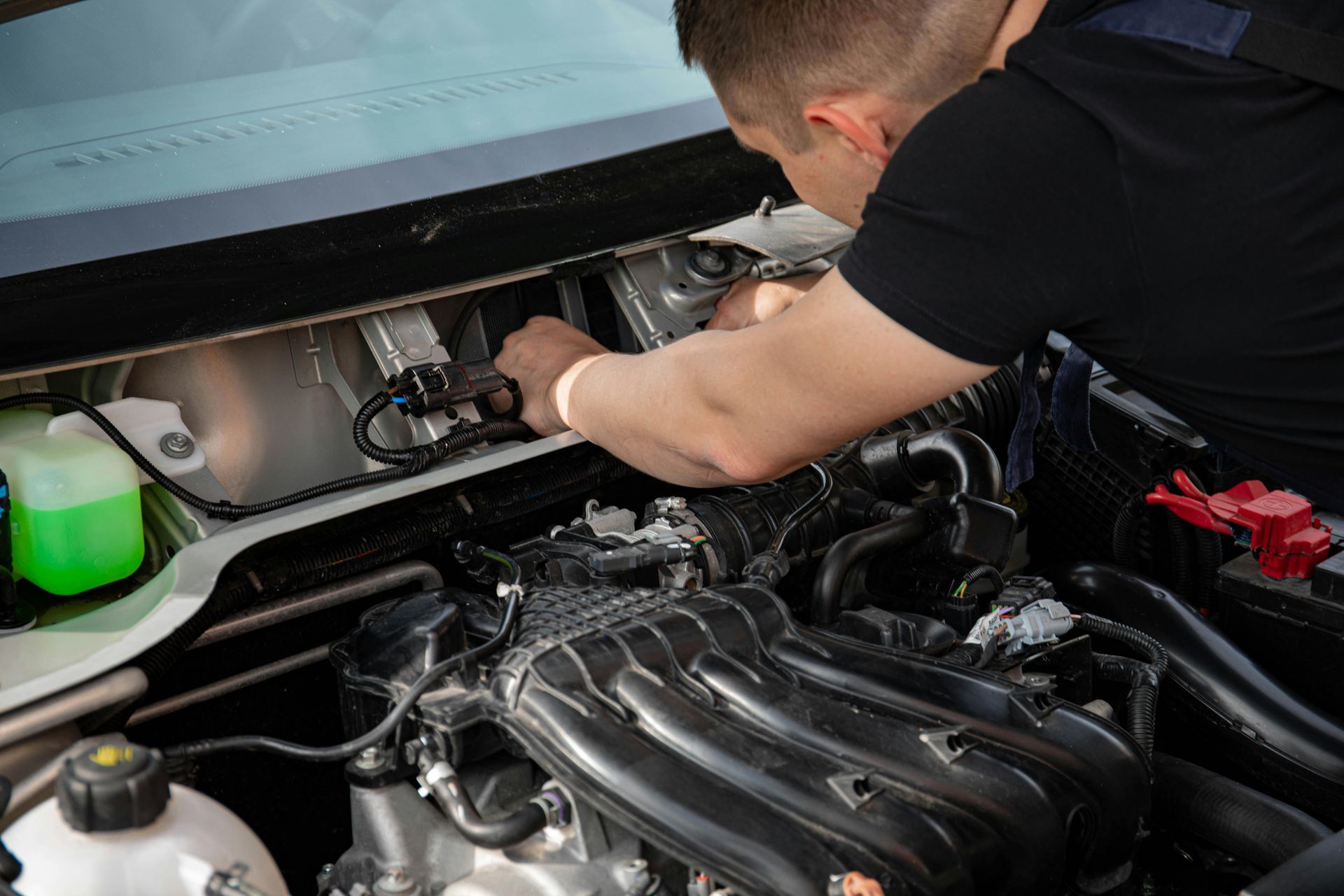 Mechanic working on a car engine, hands visible, black shirt, engine bay view.