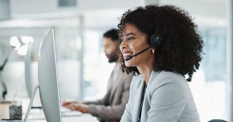 A woman wearing a headset is sitting in front of a computer.