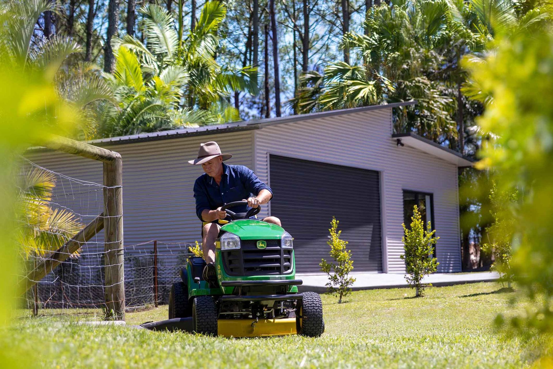 A Man Is Riding A Lawn Mower In Front Of A Shed – South Kempsey NSW - Fair Dinkum Builds Macleay Valley Sheds