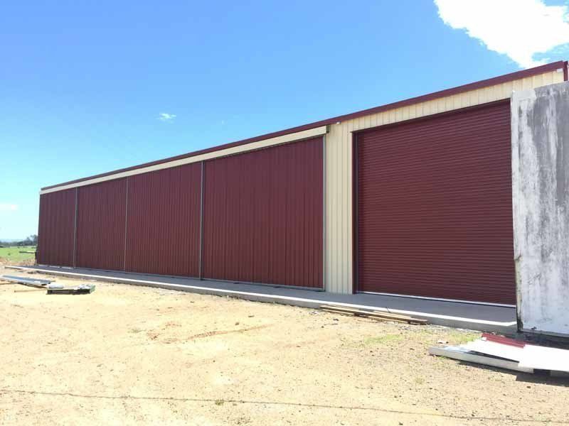 A Row Of Red Garage Doors On A Building In A Field – South Kempsey NSW - Fair Dinkum Builds Macleay Valley Sheds