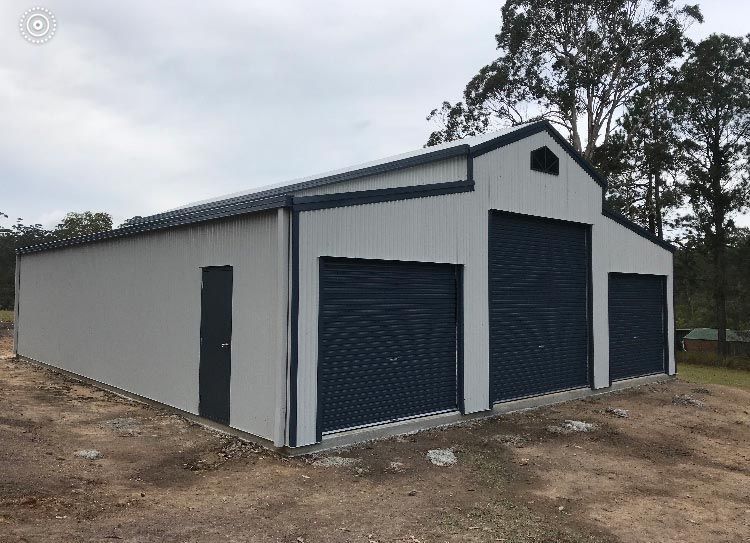 A Large White Building With Blue Garage Doors Is Sitting In The Middle Of A Dirt Field