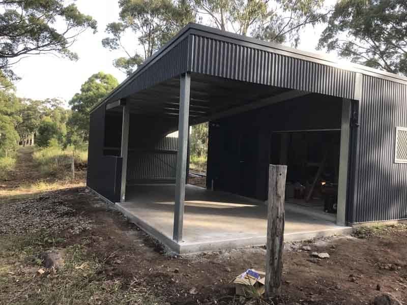 A Black Shed With A Porch Is Sitting In The Middle Of A Field – South Kempsey NSW - Fair Dinkum Builds Macleay Valley Sheds