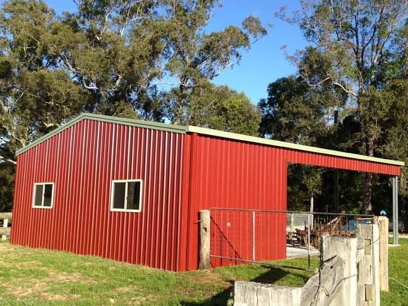 A Red Barn With A Fence And Trees In The Background – South Kempsey NSW - Fair Dinkum Builds Macleay Valley Sheds