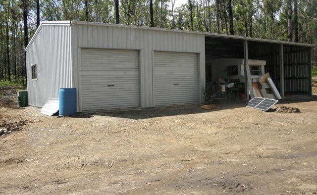 A White Building With Two Garage Doors Is Sitting In The Middle Of A Dirt Field 