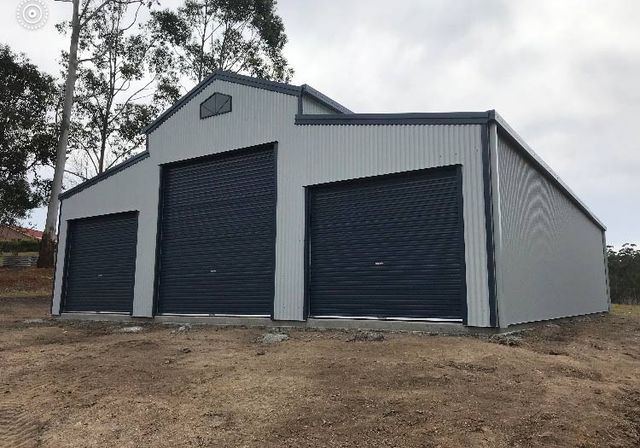 A Large Garage With Three Garage Doors Is Sitting On Top Of A Dirt Field