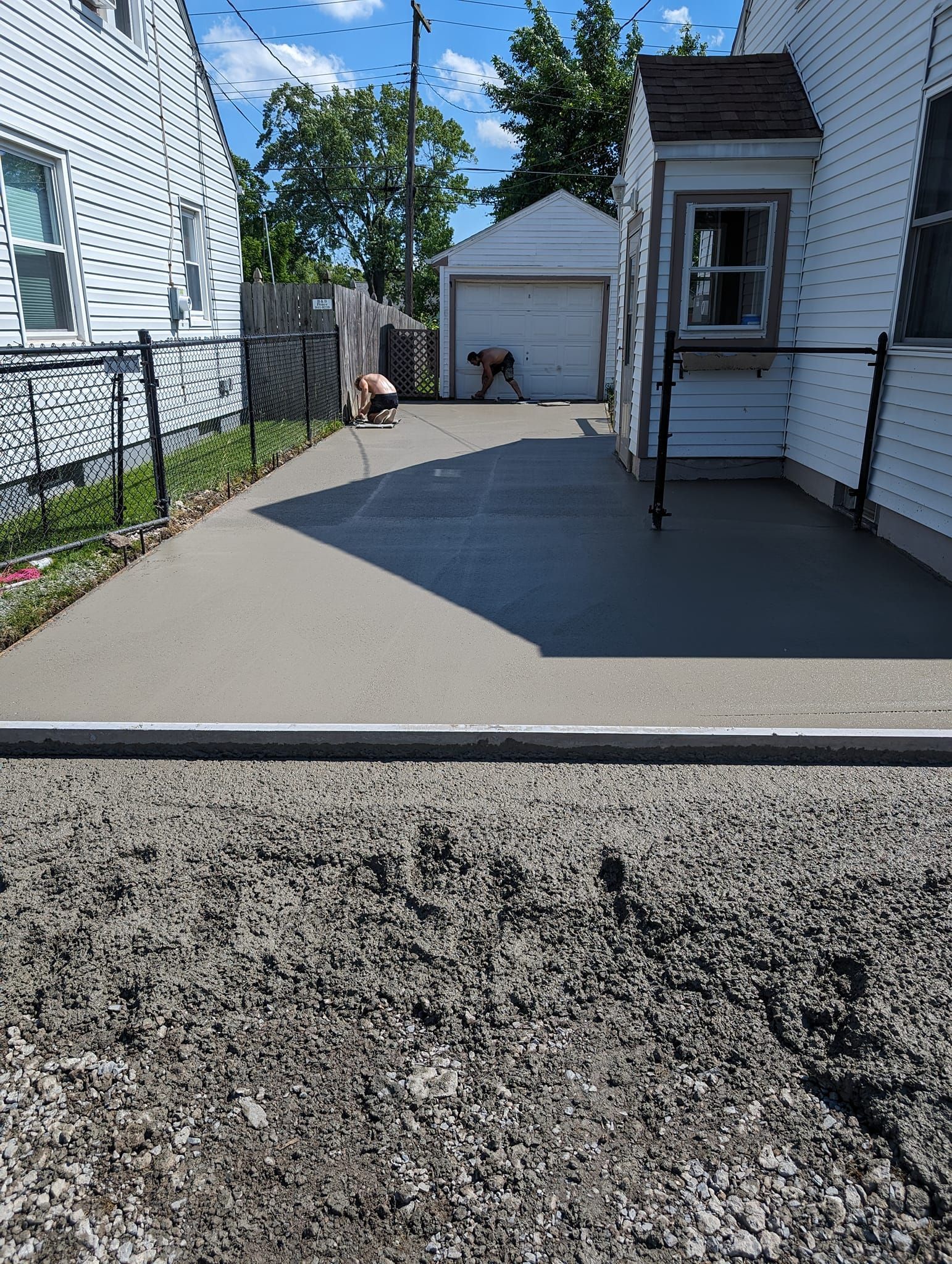 Newly poured concrete patio next to a white house and a driveway leading to a garage. Person in background.