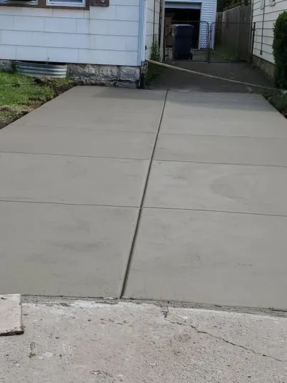 Newly poured concrete driveway in front of a white house, divided into rectangular sections.