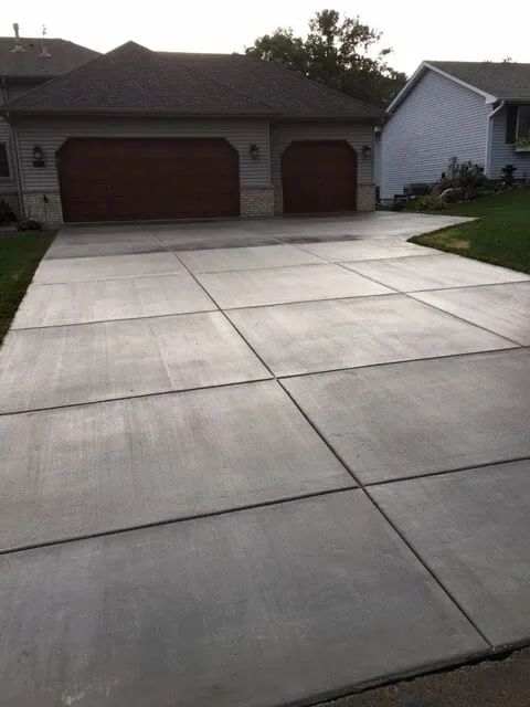 Driveway in front of a house, divided into concrete squares. Two-car garage, brown doors, green grass.