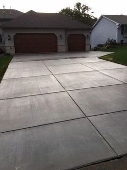 Driveway in front of a house, divided into concrete squares. Two-car garage, brown doors, green grass.