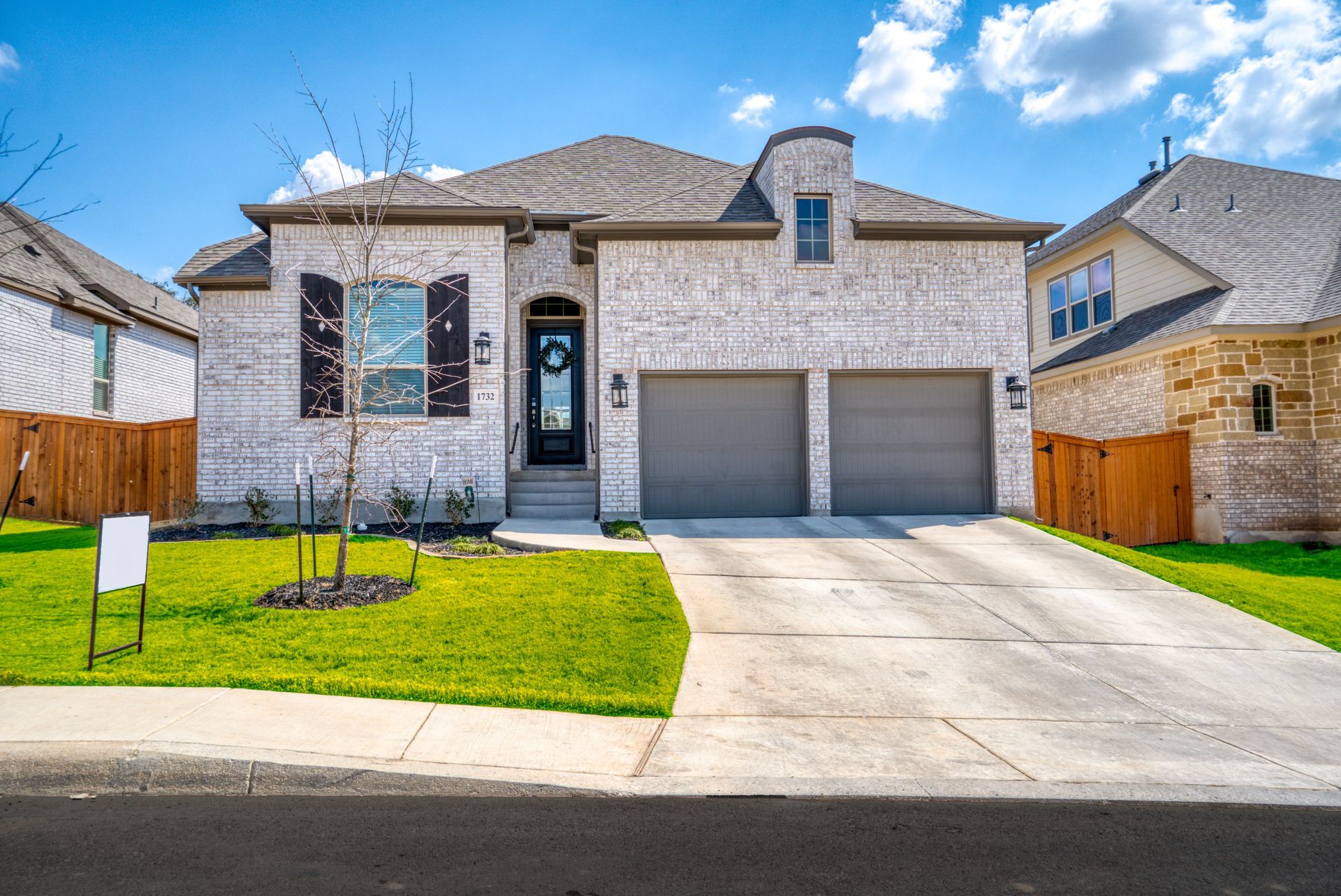 Brick house with two-car garage, green lawn, and blue sky.