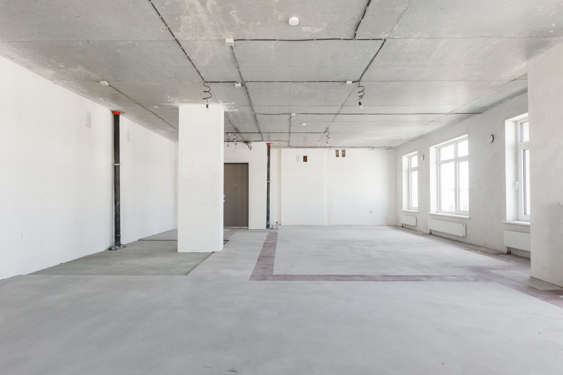 Empty, unfinished room with white walls, concrete floor and ceiling, several windows.