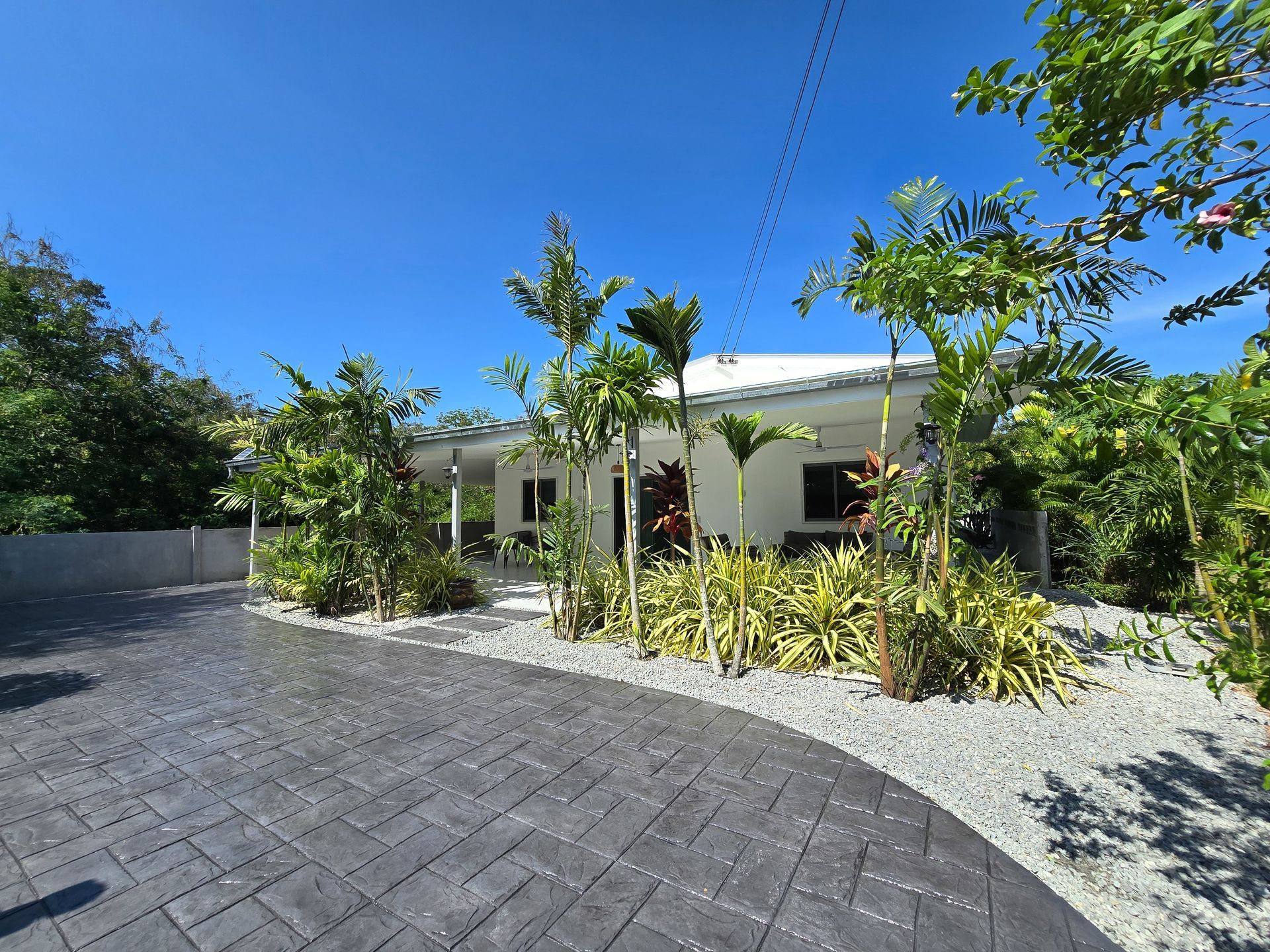 White house with a gray patterned driveway, surrounded by greenery under a blue sky.