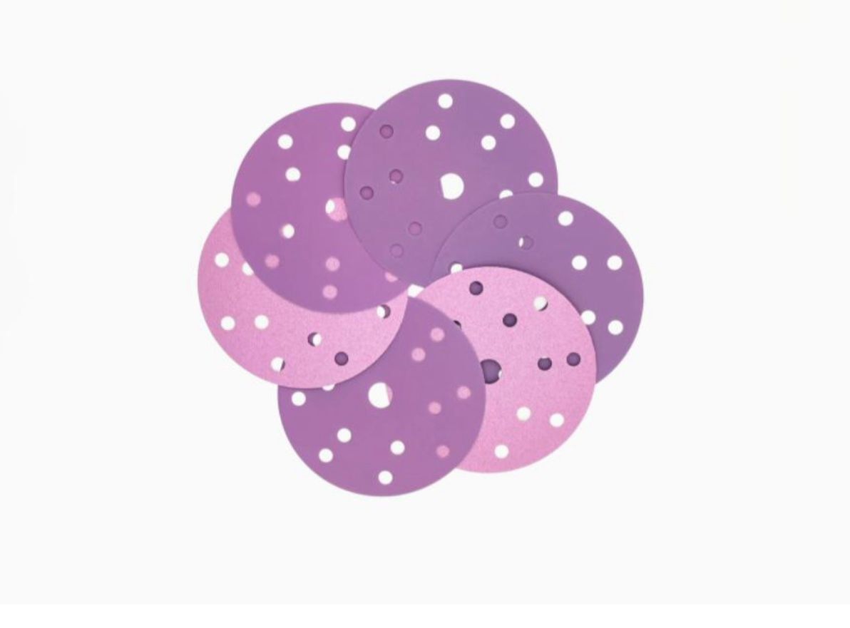 Purple and pink sanding discs with multiple holes arranged in a flower-like pattern.