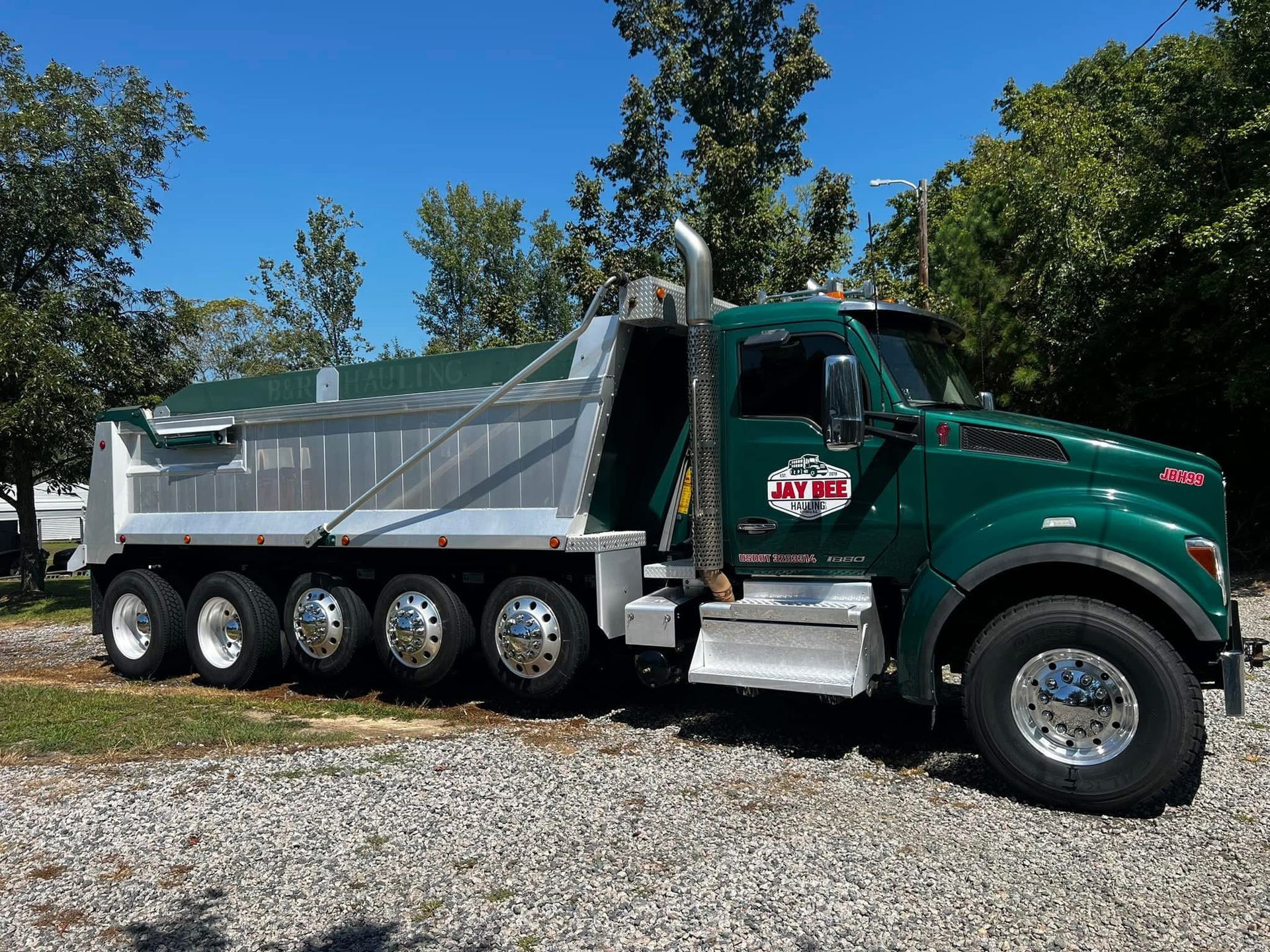 A green dump truck is parked in a gravel lot