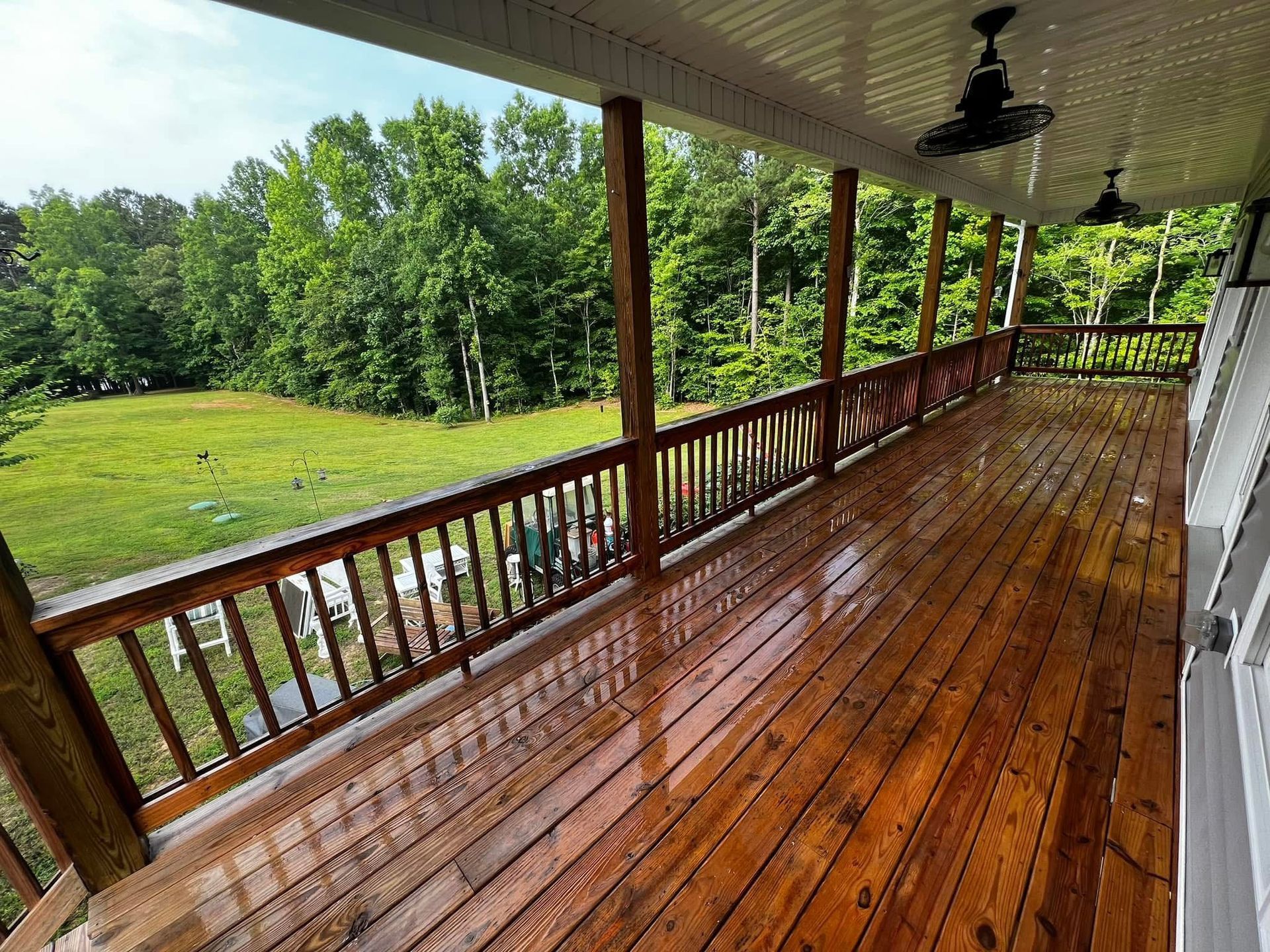A large wooden deck with a ceiling fan and a view of a field.