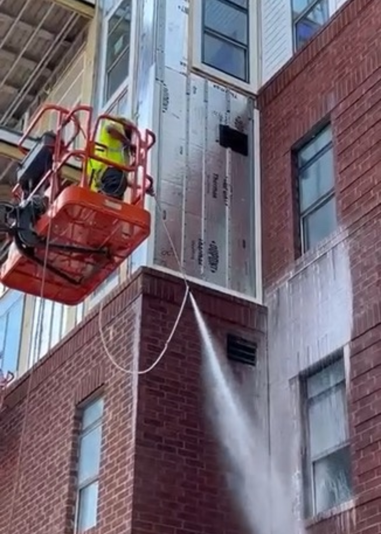 A machine is spraying water on the side of a brick building.