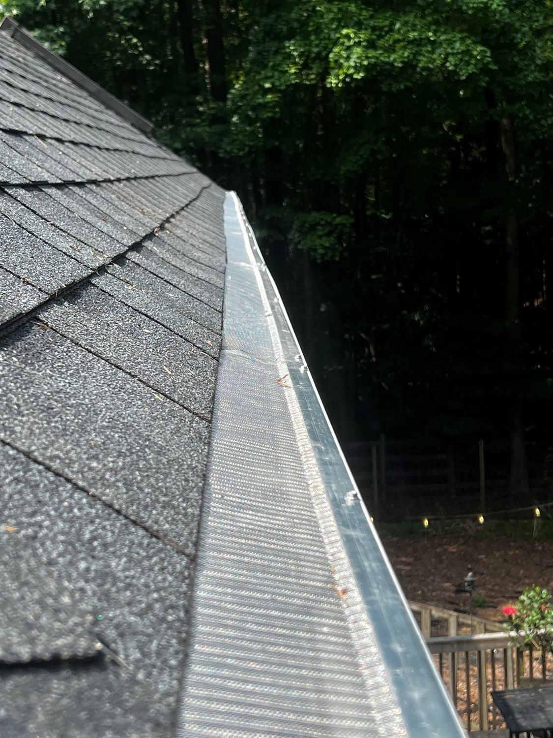 A close up of a gutter on a roof with trees in the background.