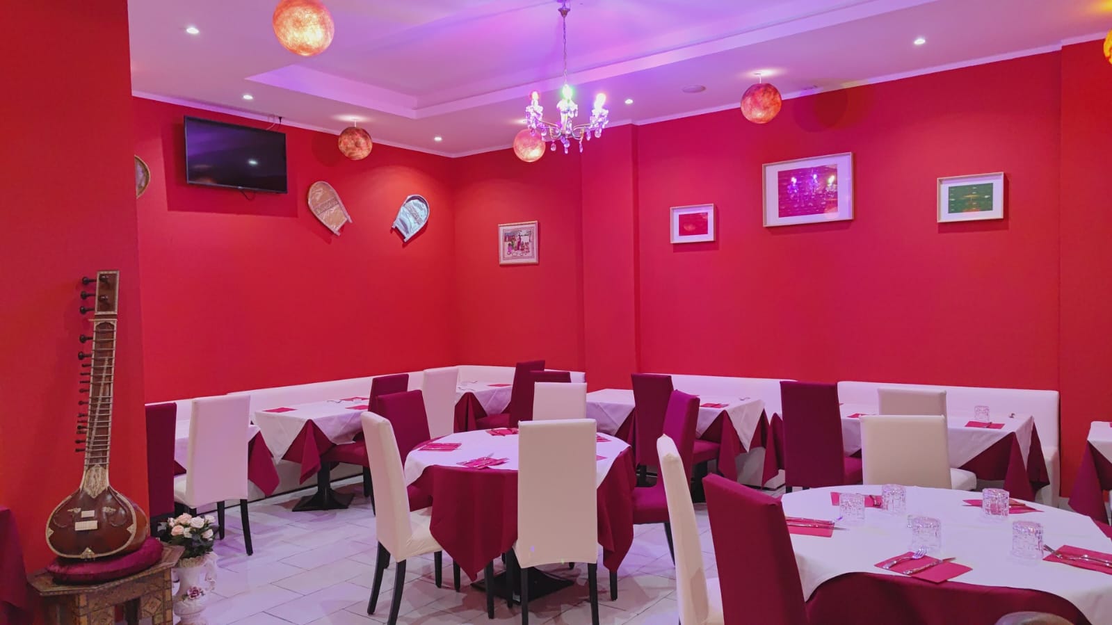 Sala più grande con tavoli di diversa forma, apparecchiati con tovaglia rossa e sedie di colore bianco