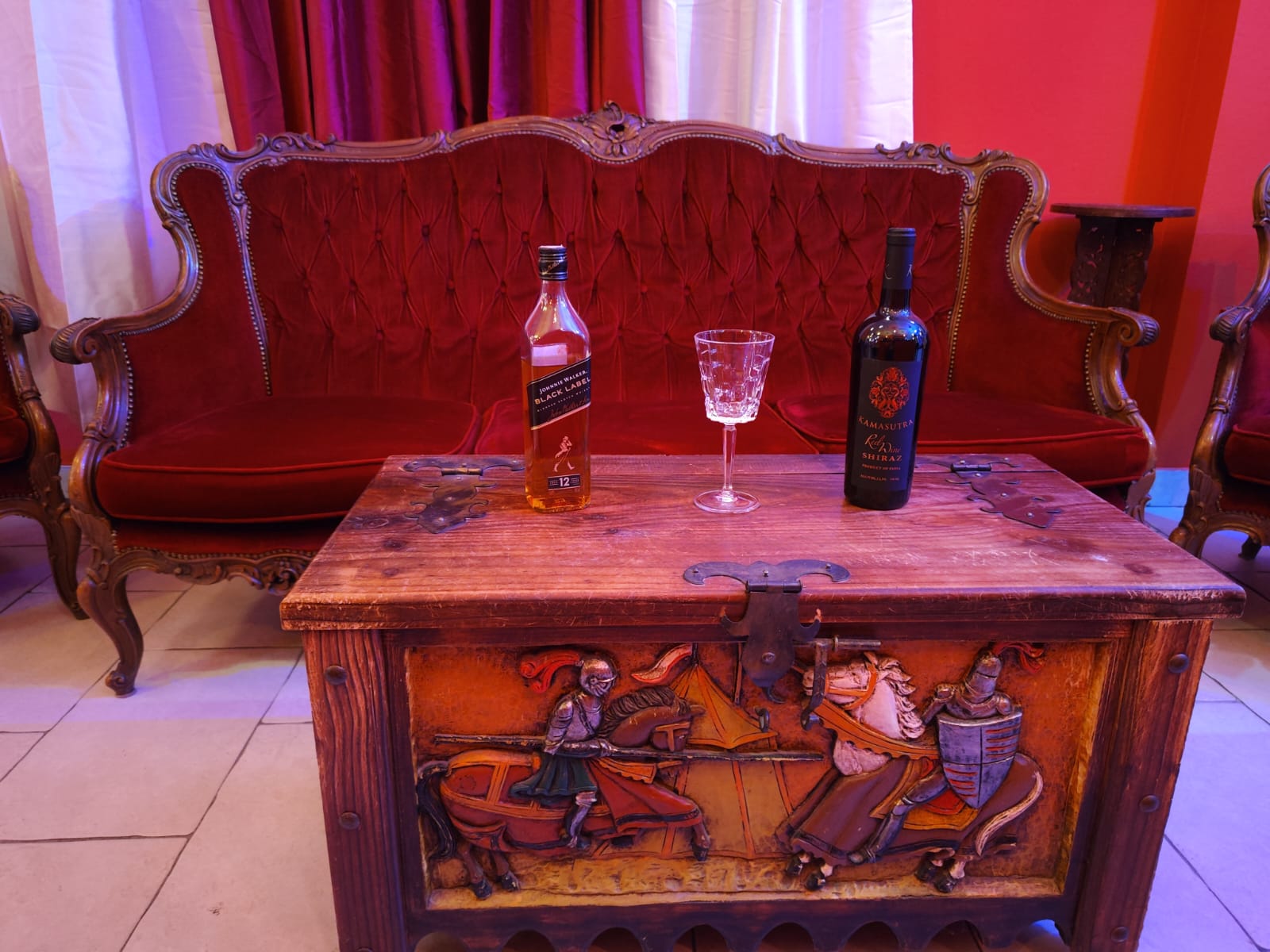 tavolino orientale in legno con sopra dei liquori e sullo sfondo un divano di colore rosso