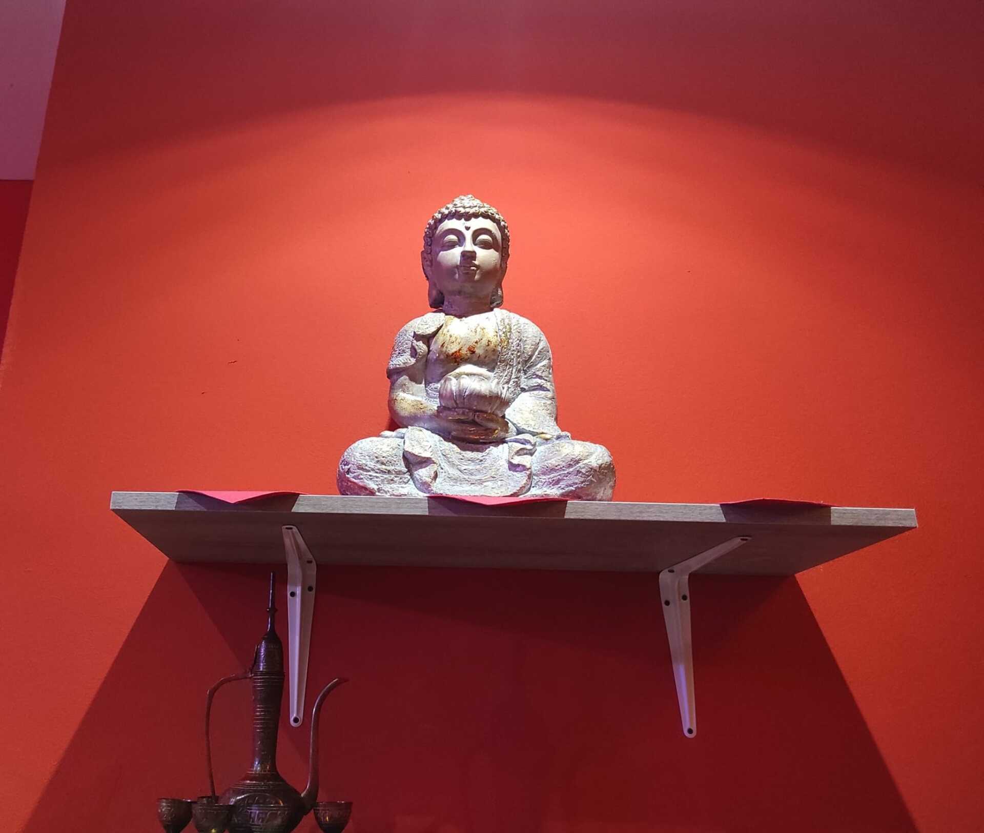 statua del Buddah su mensola bianca e parete rossa