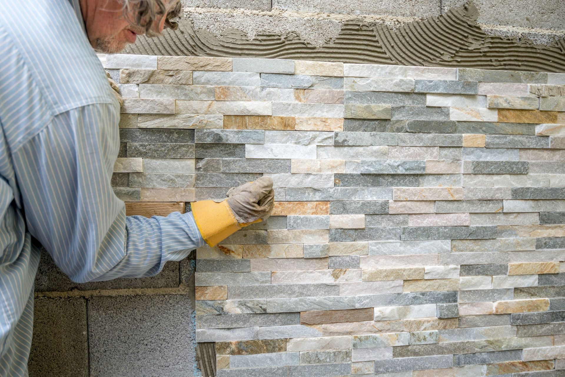 Man laying decorative stone tiles on a wall, using gloved hand to position the pieces.