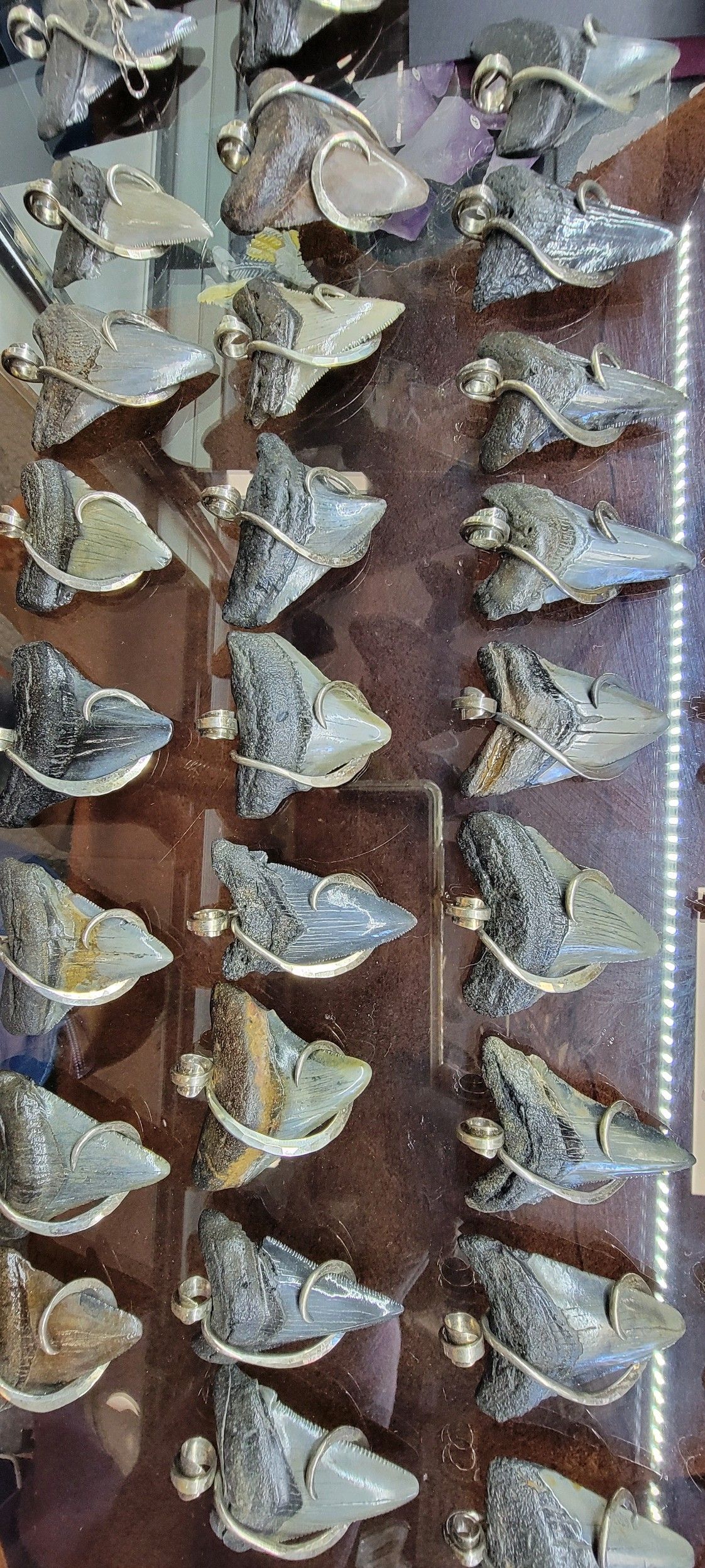Display case filled with numerous small, gray, abstract metal sculptures, possibly jewelry.