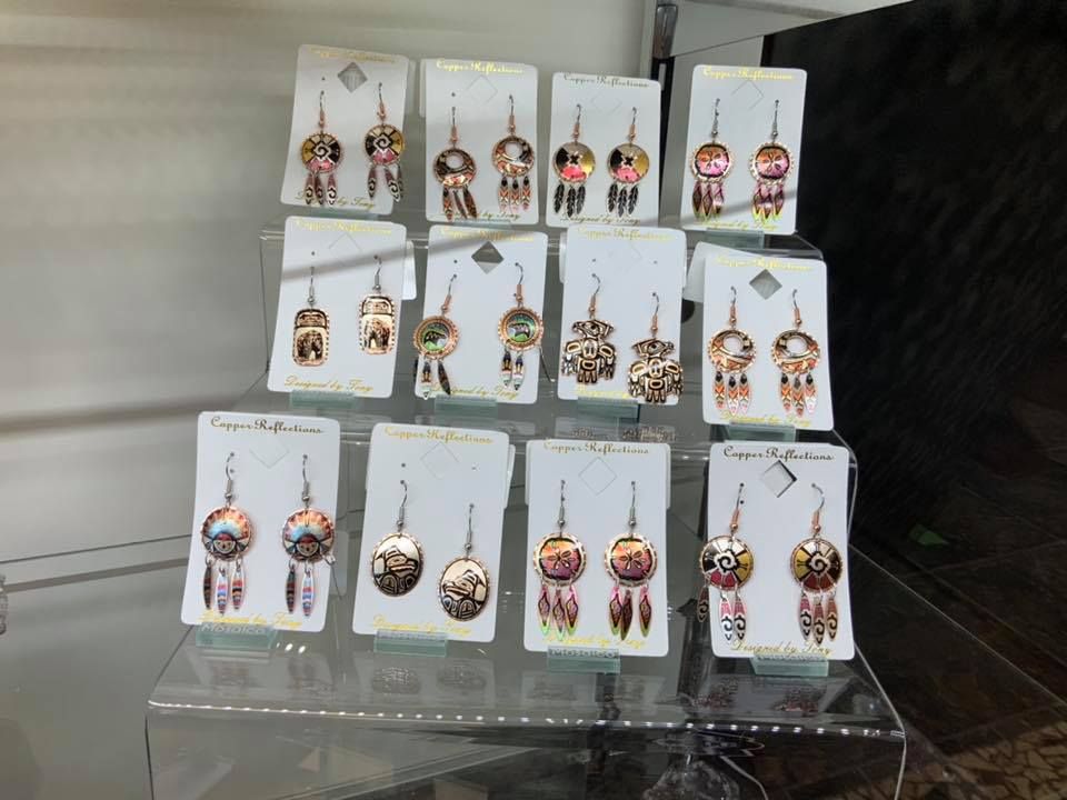 Earrings on display, copper-colored with dreamcatcher designs, arranged on tiered shelves.