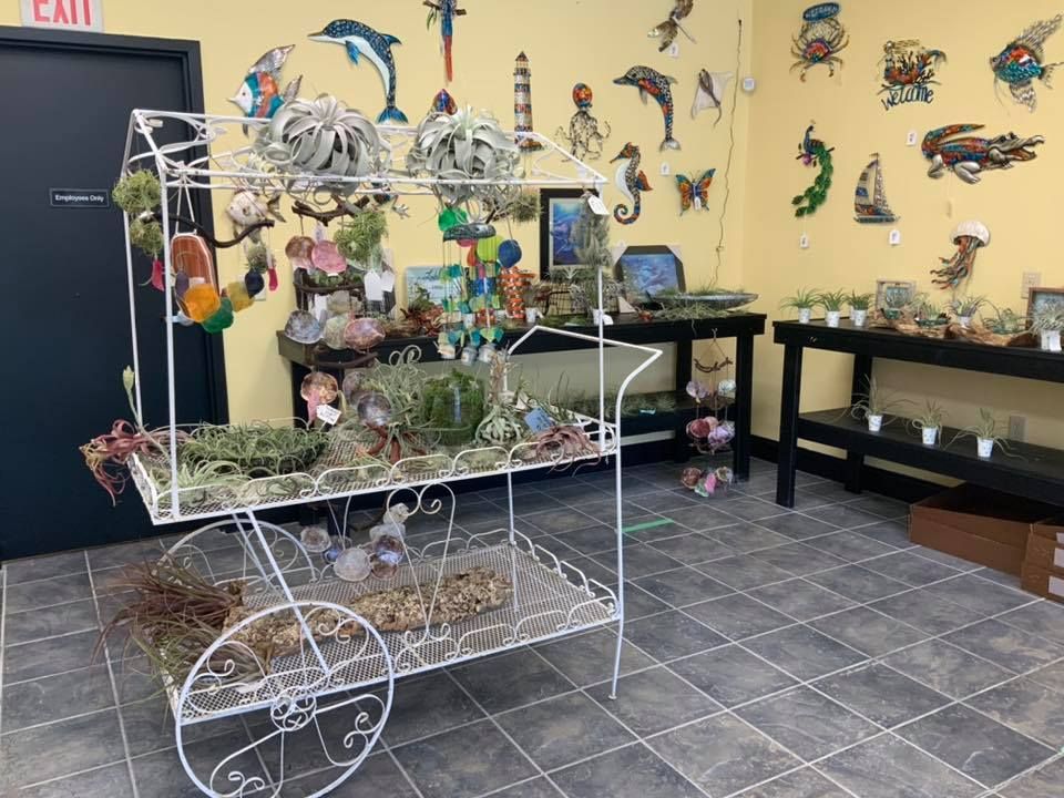 A white plant cart with various plants and decorations inside a shop with a yellow wall and artwork.