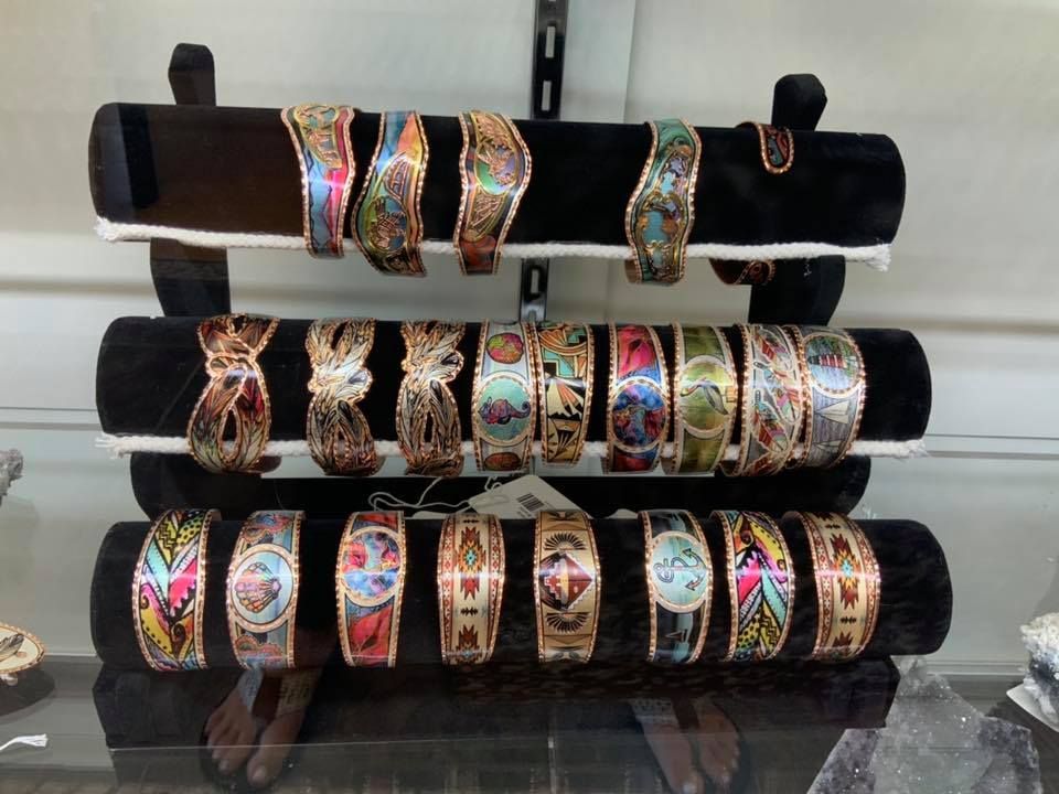 Display of colorful, engraved copper bracelets on a tiered black velvet stand.