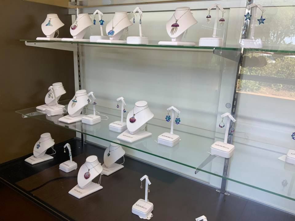 Jewelry display case with necklaces and earrings on white stands, with a brown wall background.
