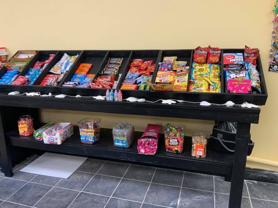 Black candy display stand with various snacks in a room with tiled floors and a pale yellow wall.