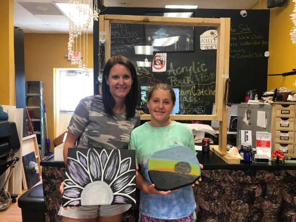 Woman and girl holding painted canvases in a craft store in a USA shop.