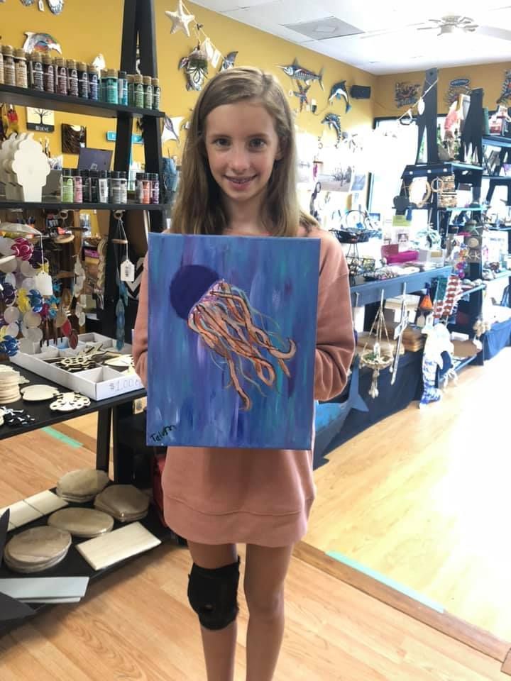 Young girl smiling, holding a blue jellyfish painting in a craft store in a USA shop.