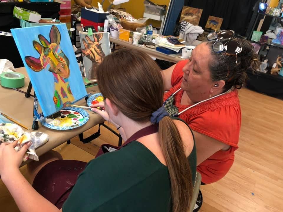Two women painting giraffes together in a brightly lit studio in a USA shop.