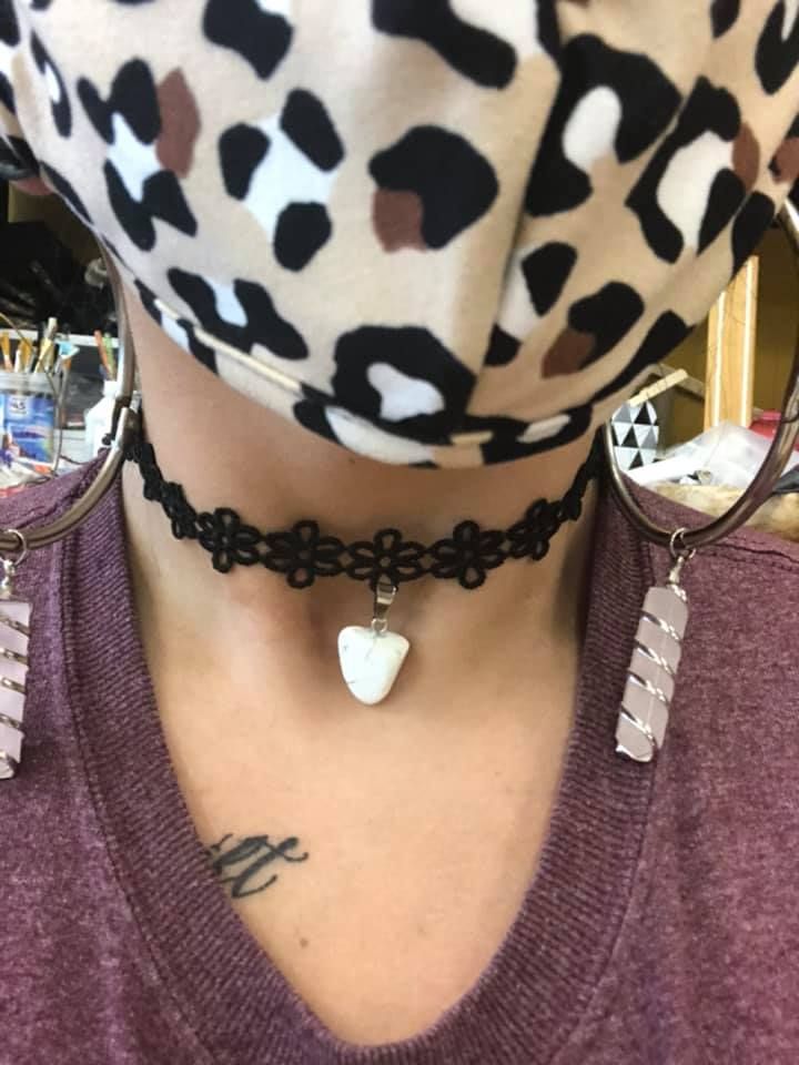 Person wearing a leopard-print face mask, black lace choker with a heart pendant, and hoop earrings with rectangular crystal charms in a USA shop.
