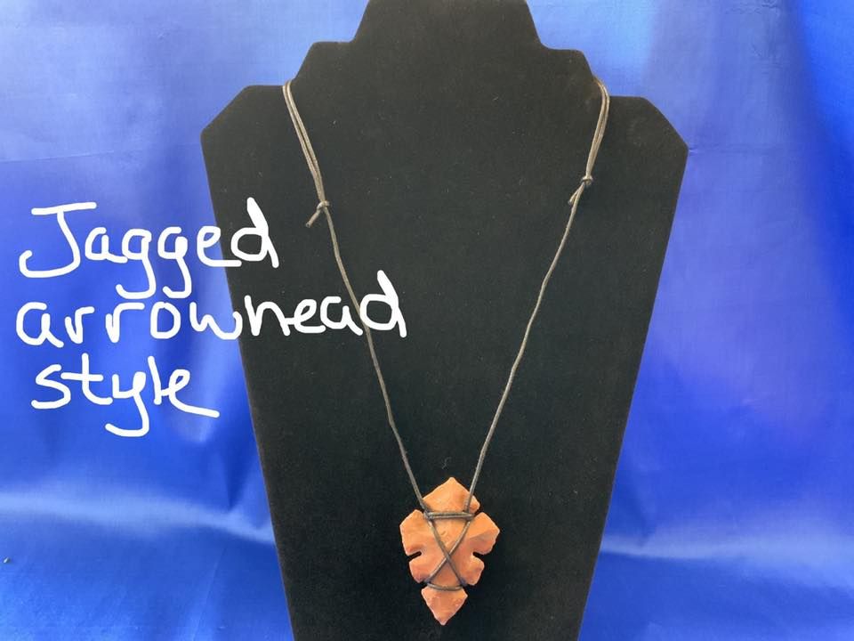 Jagged arrowhead pendant necklace displayed on a black stand against a blue background in a USA shop.
