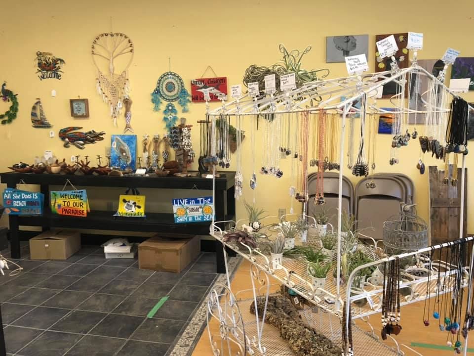 Inside a shop, art and jewelry display on walls and shelves against a yellow wall in a USA shop.