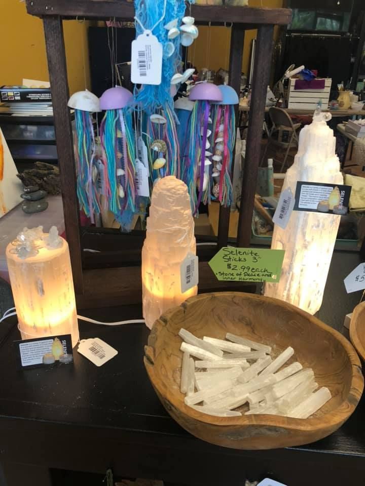 Display of lit selenite lamps, a wooden bowl of selenite shards, and colorful jellyfish mobiles in a USA shop.