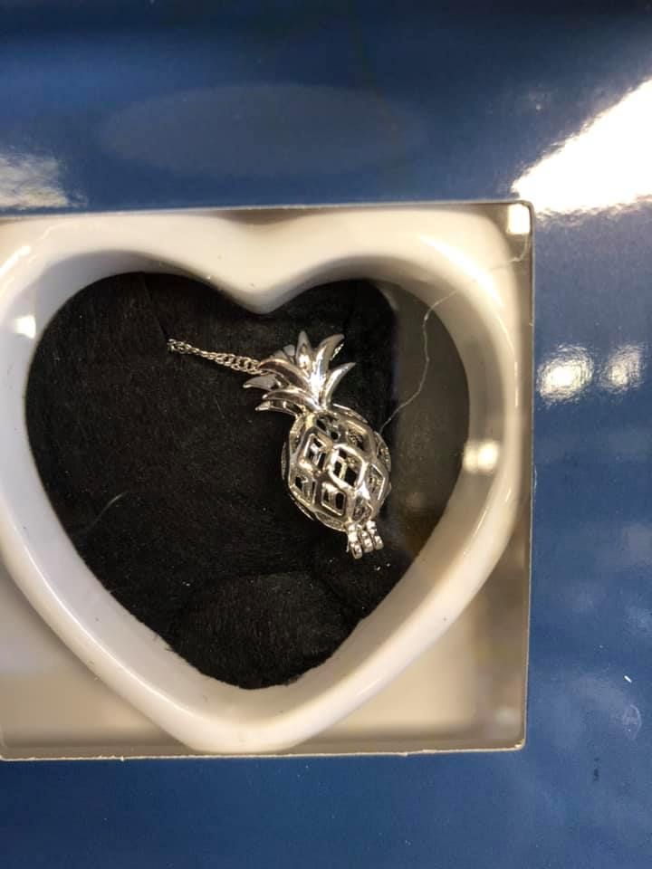Silver pineapple-shaped pendant inside a white heart-shaped box on a blue surface in a USA shop.