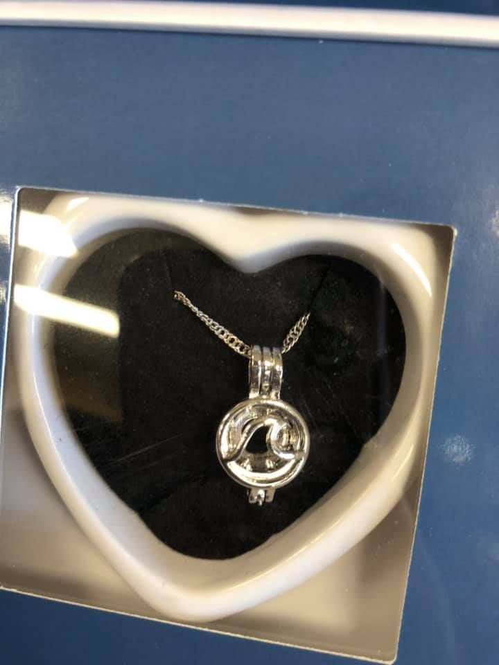 Silver pendant necklace inside a white heart-shaped box with a black interior on a blue surface in a USA shop.
