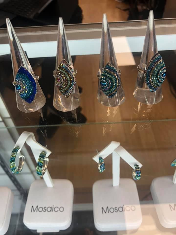 Jewelry display: earrings and rings with blue and green gems on white stands, labeled 