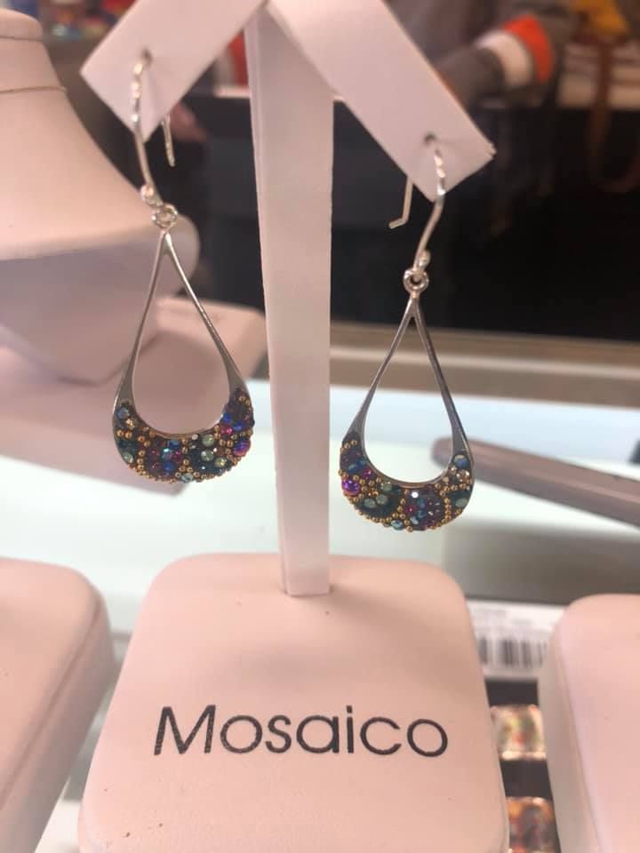 Teardrop earrings on display; silver frame with mosaic of colorful gems; Mosaic logo on base in a USA shop.