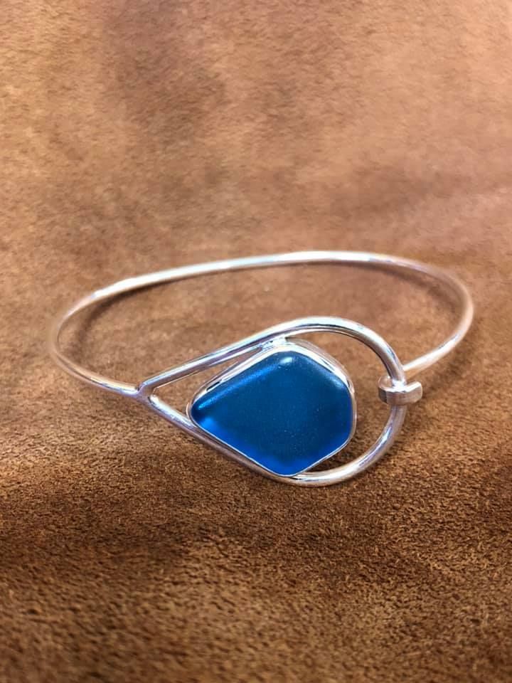 Silver bangle bracelet with a teardrop-shaped setting holding a blue, diamond-shaped stone in a USA shop.