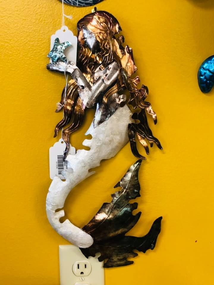 Metal mermaid wall decor with copper, silver, and white finish against a yellow wall.